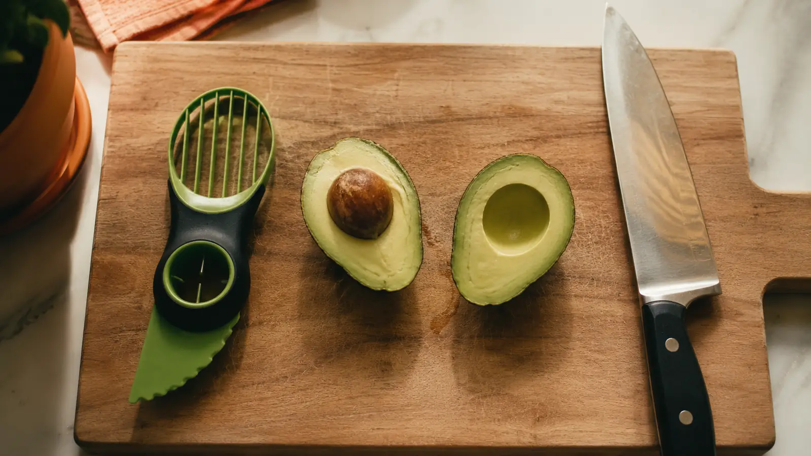 NADOBA 3-in-1 avocado tool laid next to a chef's knife on a wood cutting board with a halved avocado between them