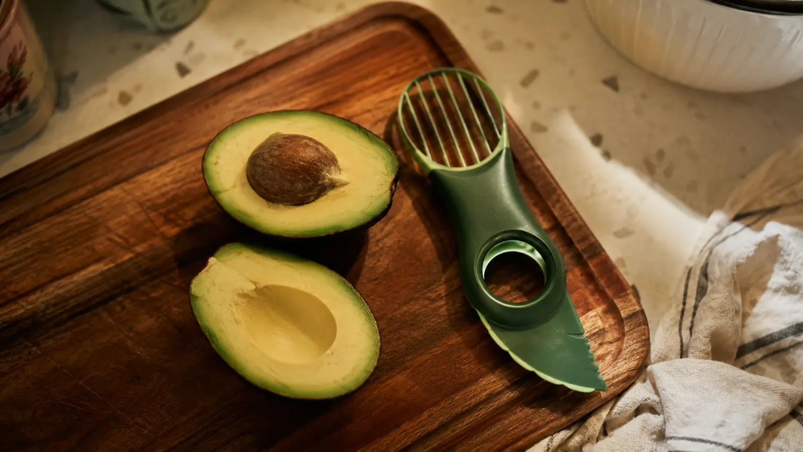 Halved avocados on a wood cutting board next to a NADOBA 3-in-1 avocado tool in morning kitchen light