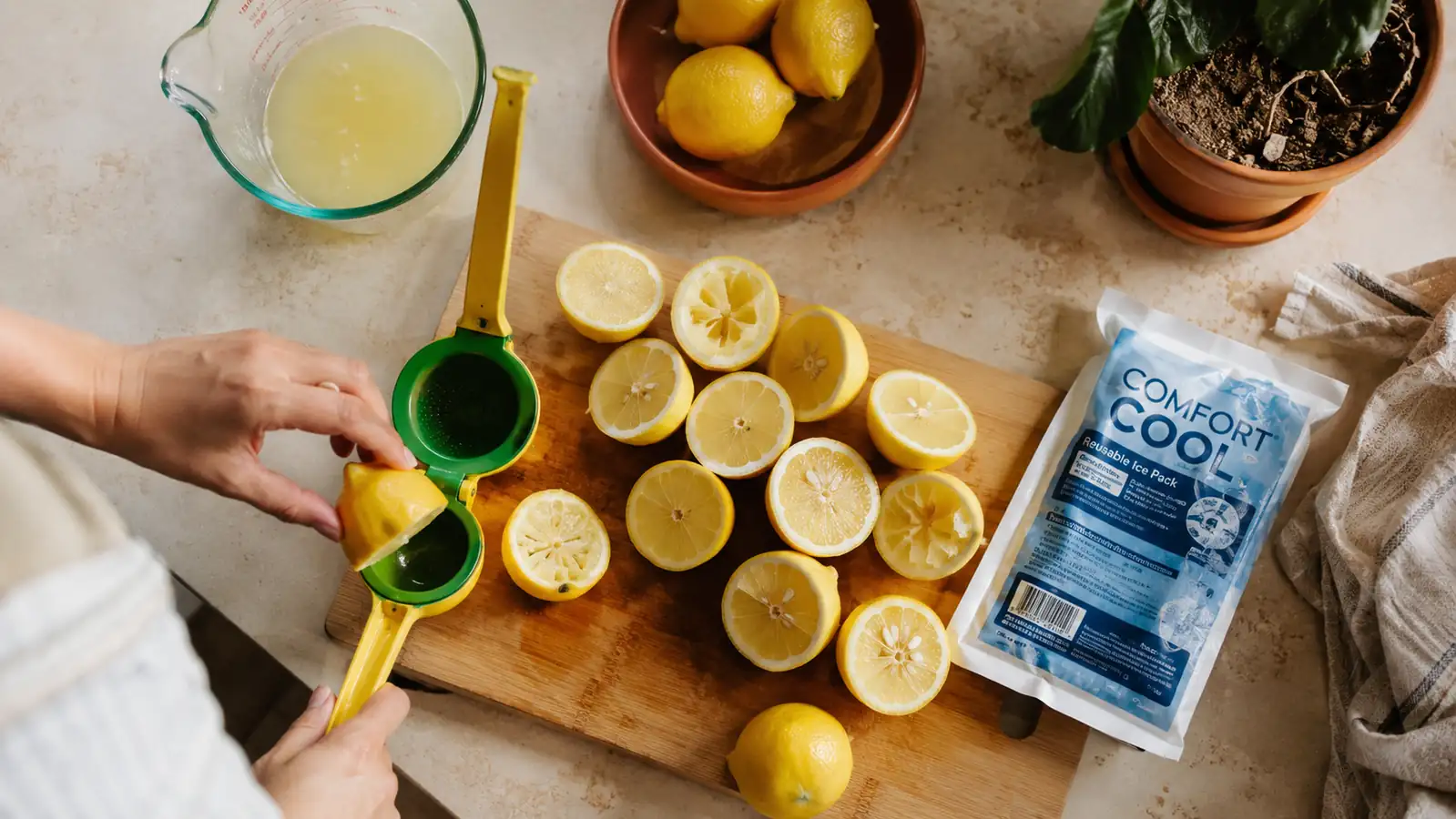 A kitchen counter with a dozen halved lemons, a small yellow and green metal lemon squeezer, and a wrist ice pack resting nearby in warm afternoon light