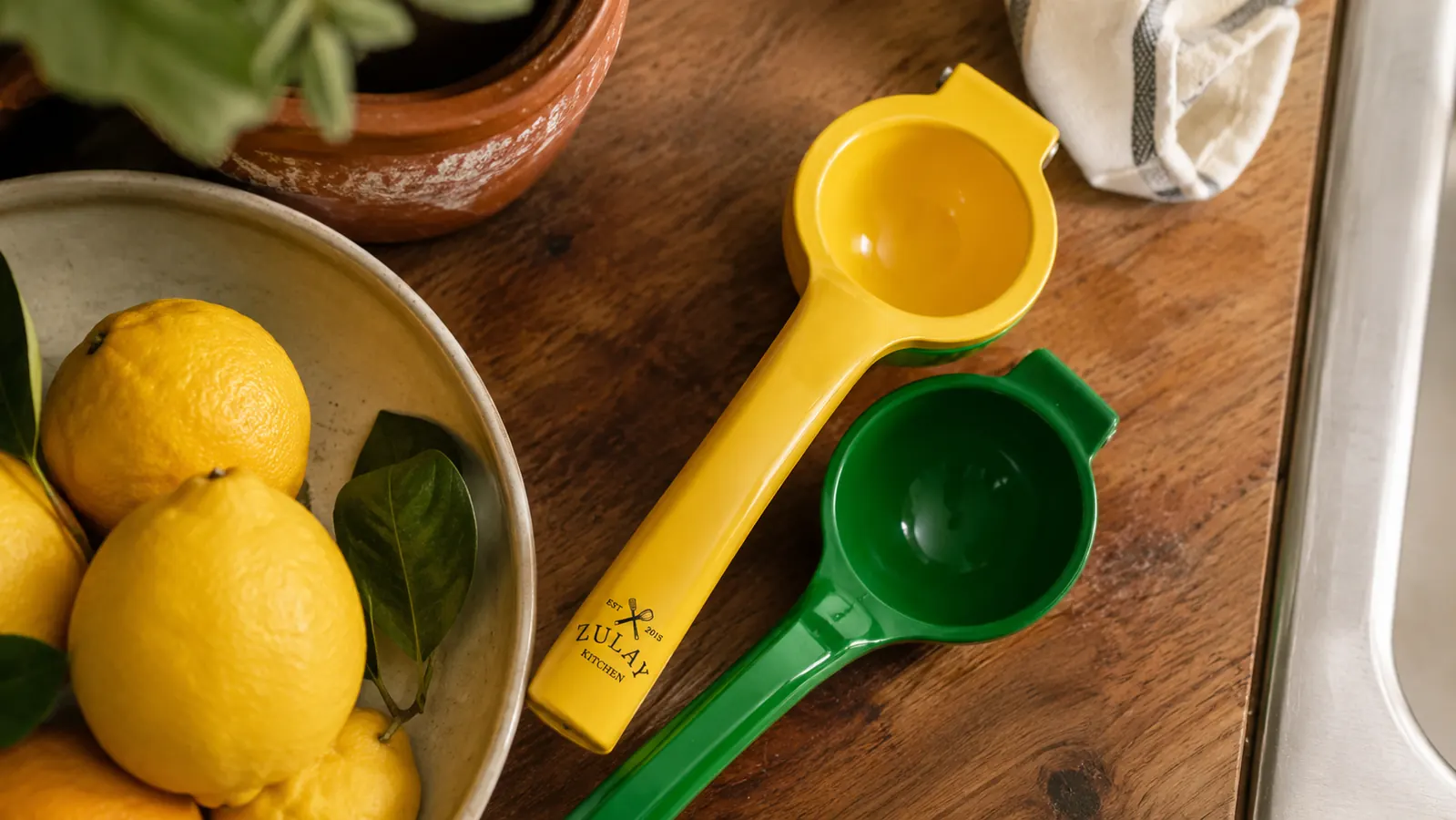Zulay metal lemon squeezer sitting open on a kitchen counter next to a bowl of whole lemons