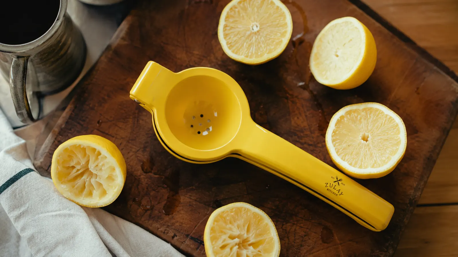 Zulay metal lemon squeezer on a wood cutting board surrounded by halved lemons in morning kitchen light