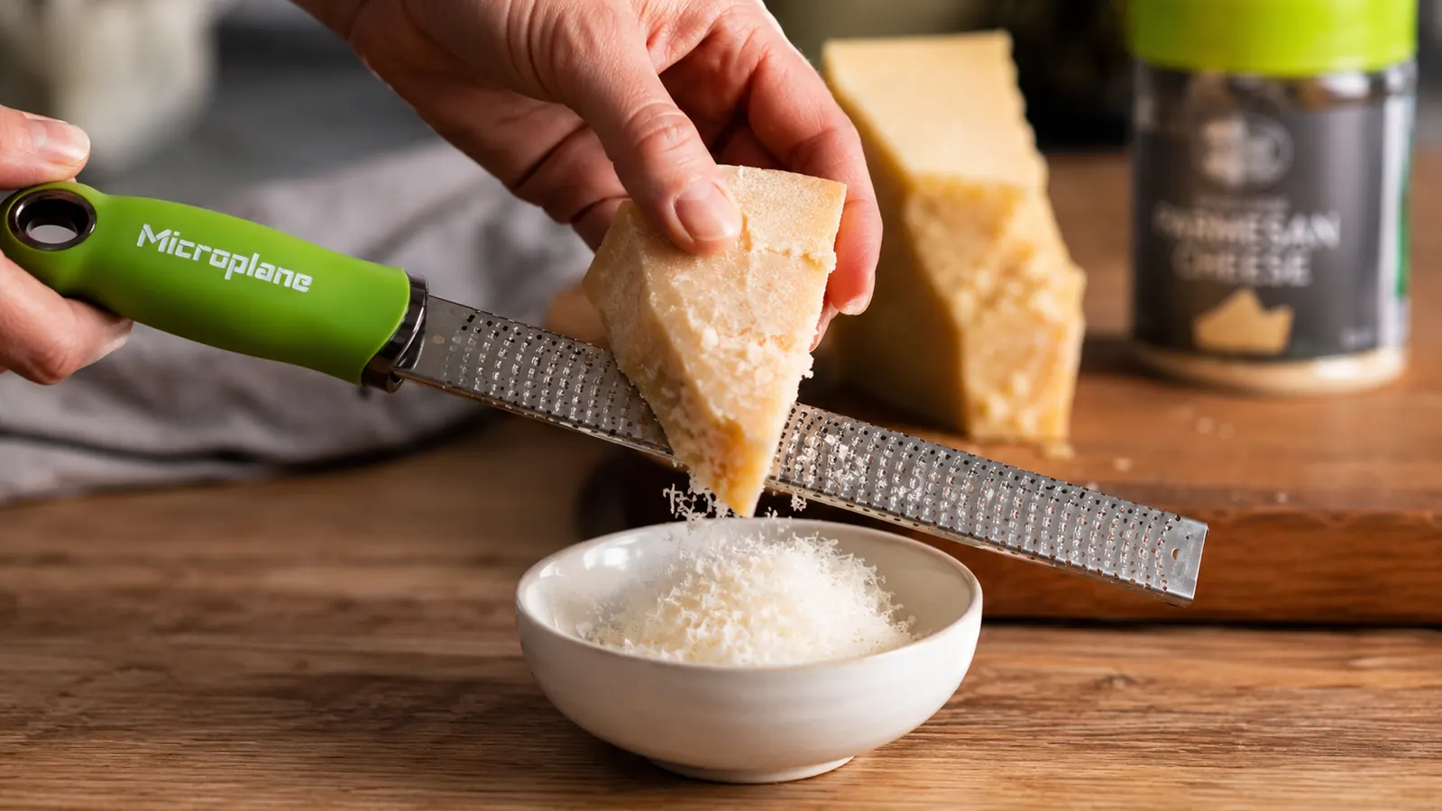 A hand grating a wedge of Parmigiano-Reggiano cheese into a light, fluffy pile using the Microplane zester