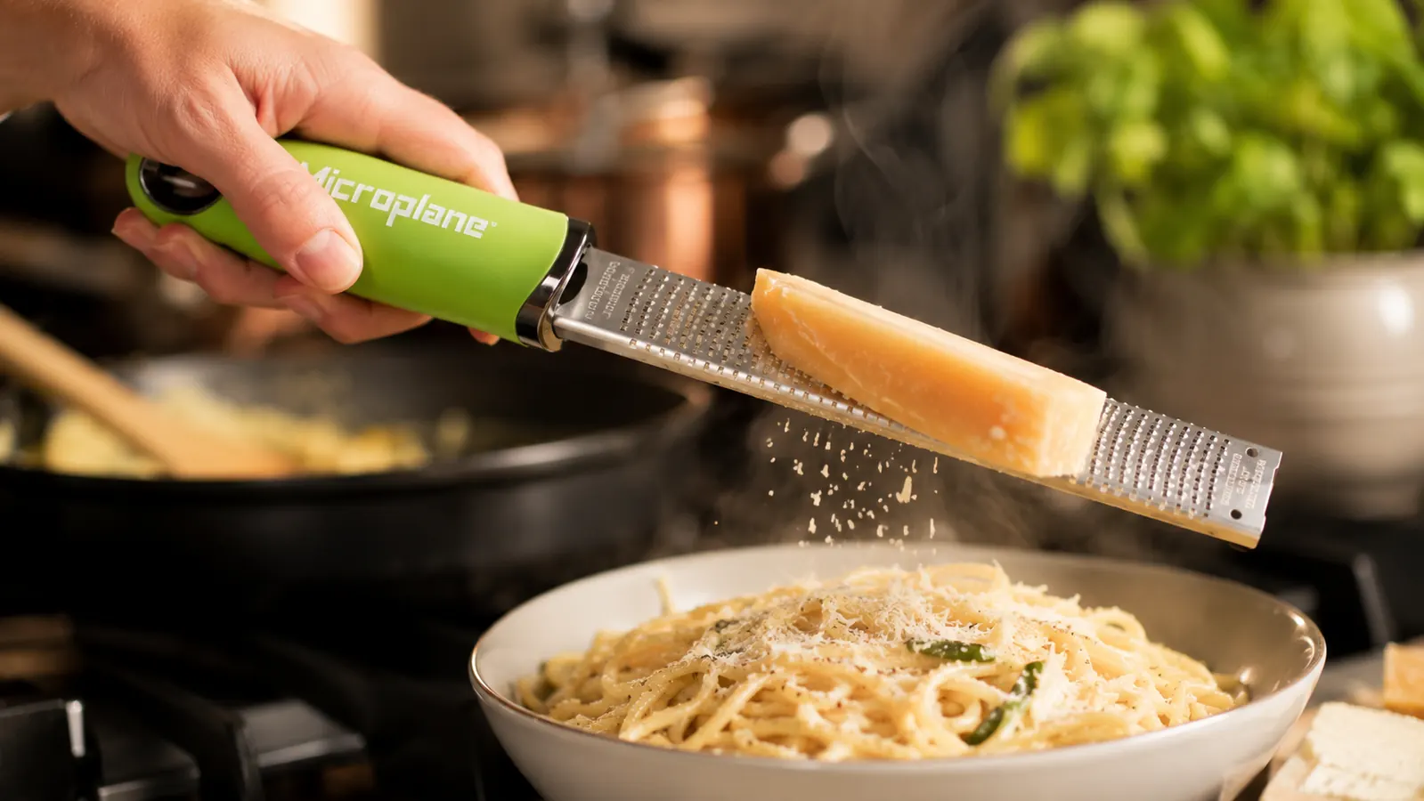 Hand grating a block of Parmesan cheese with the Microplane zester directly over a bowl of pasta