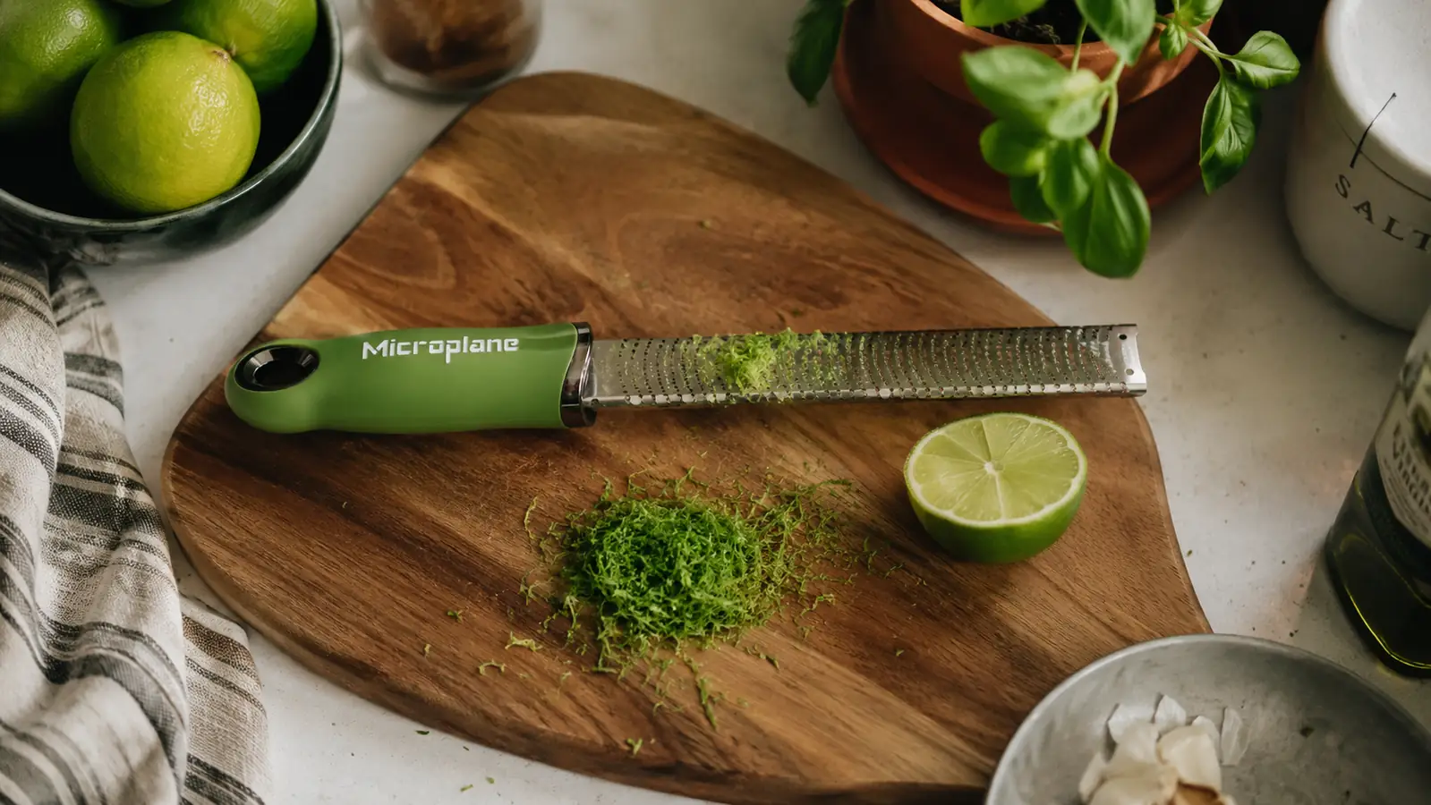 Microplane Premium Classic zester with fresh lime zest curling off the blade onto a wood cutting board
