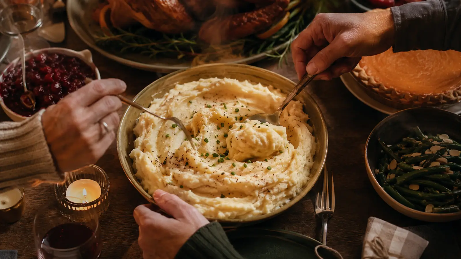 A big bowl of smooth, fluffy mashed potatoes on a set holiday table with warm evening light