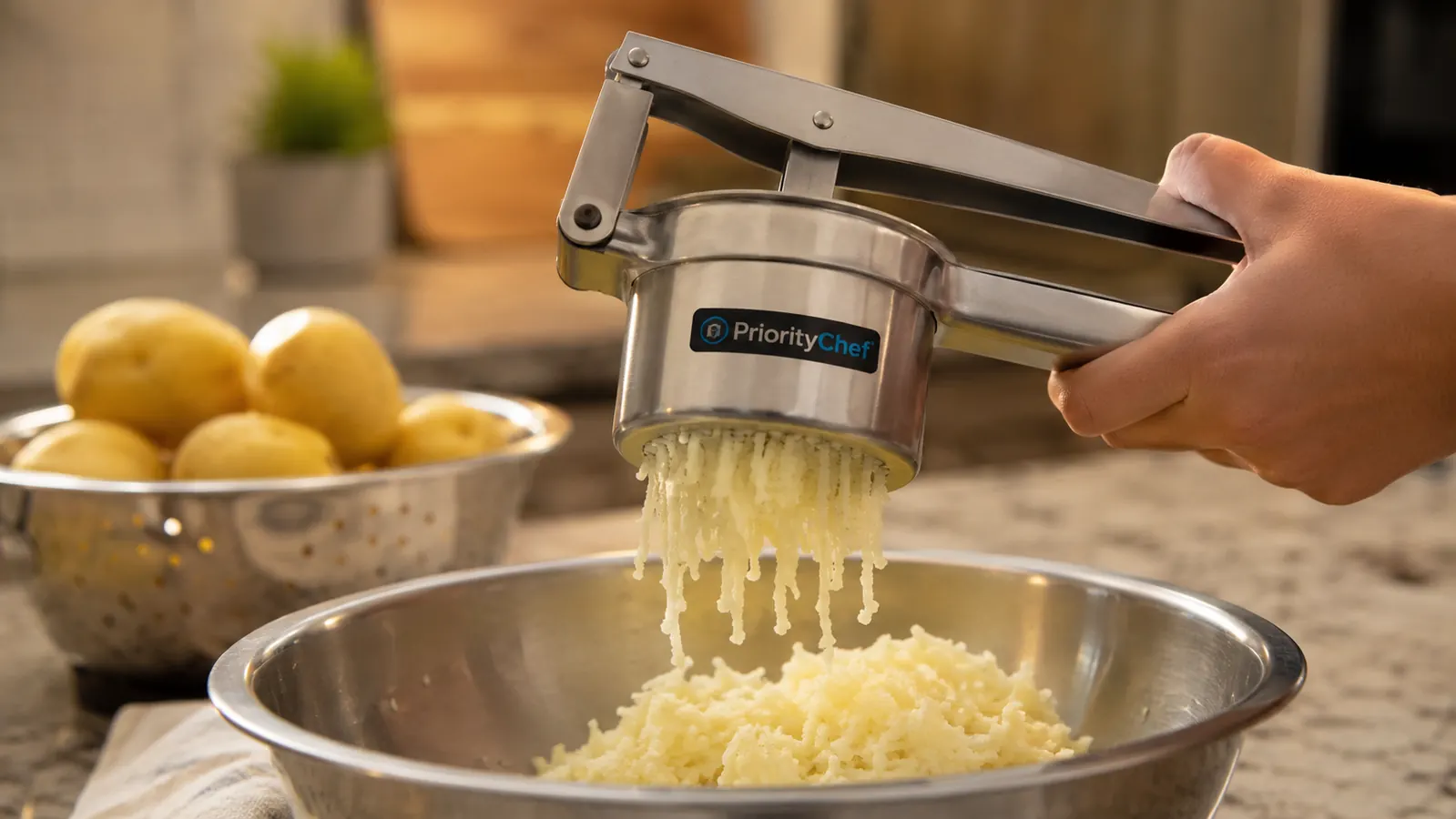 Hand squeezing the PriorityChef potato ricer over a stainless steel bowl, potato ribbons falling through the holes